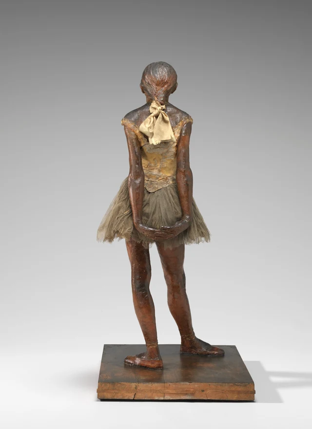 Full-length rear view of the same wax sculpture. A pale satin ribbon is tied at the back of the hair. The arms descend beside the torso and draw back, with the hands clasped behind the gauze skirt.